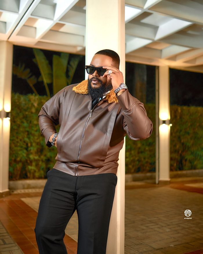 Whitemoney in a brown leather jacket beside a pillar at night