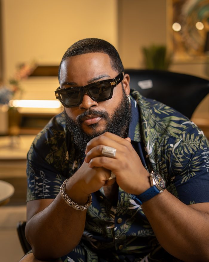 Whitemoney in a dark botanical shirt, hands clasped