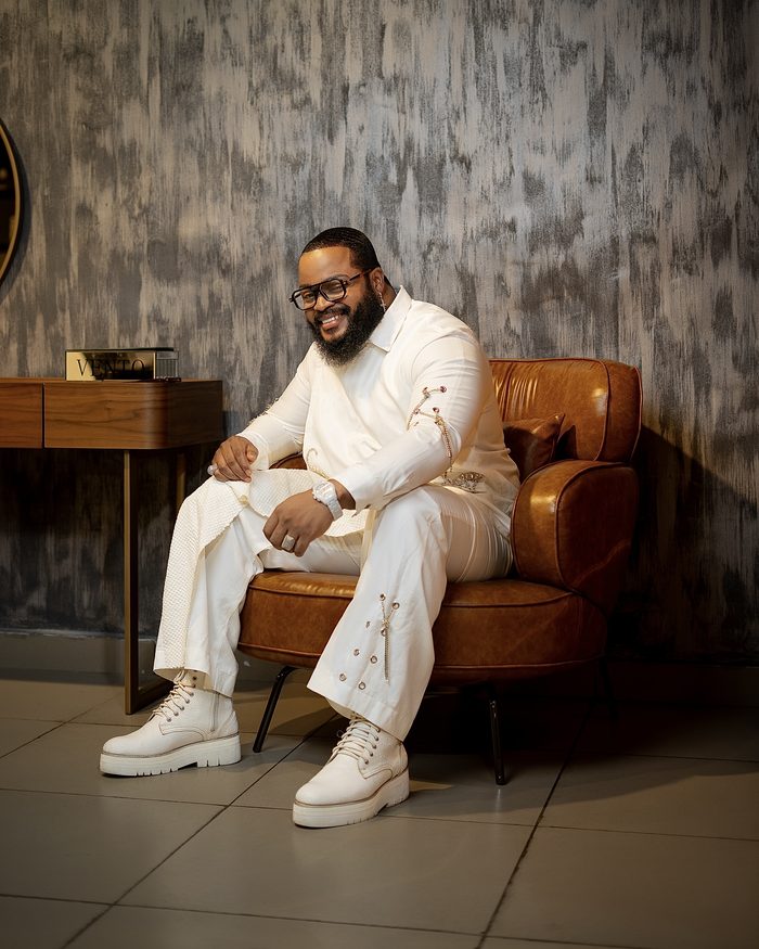 Whitemoney in a white suit seated in a tan leather armchair