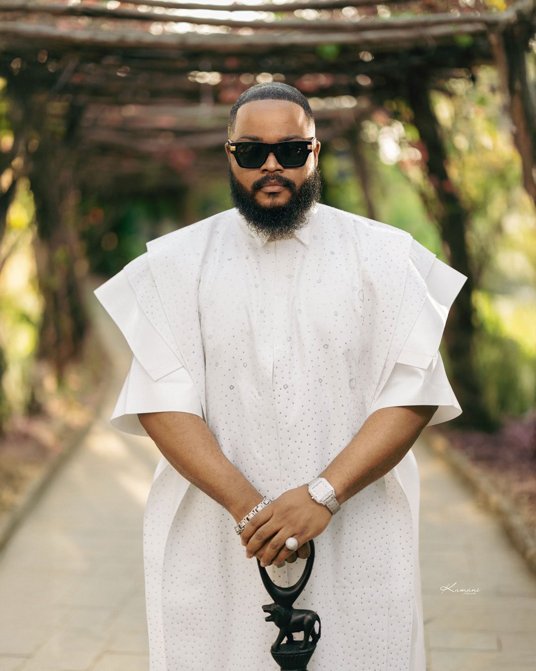 Whitemoney in a white agbada holding a carved elephant staff